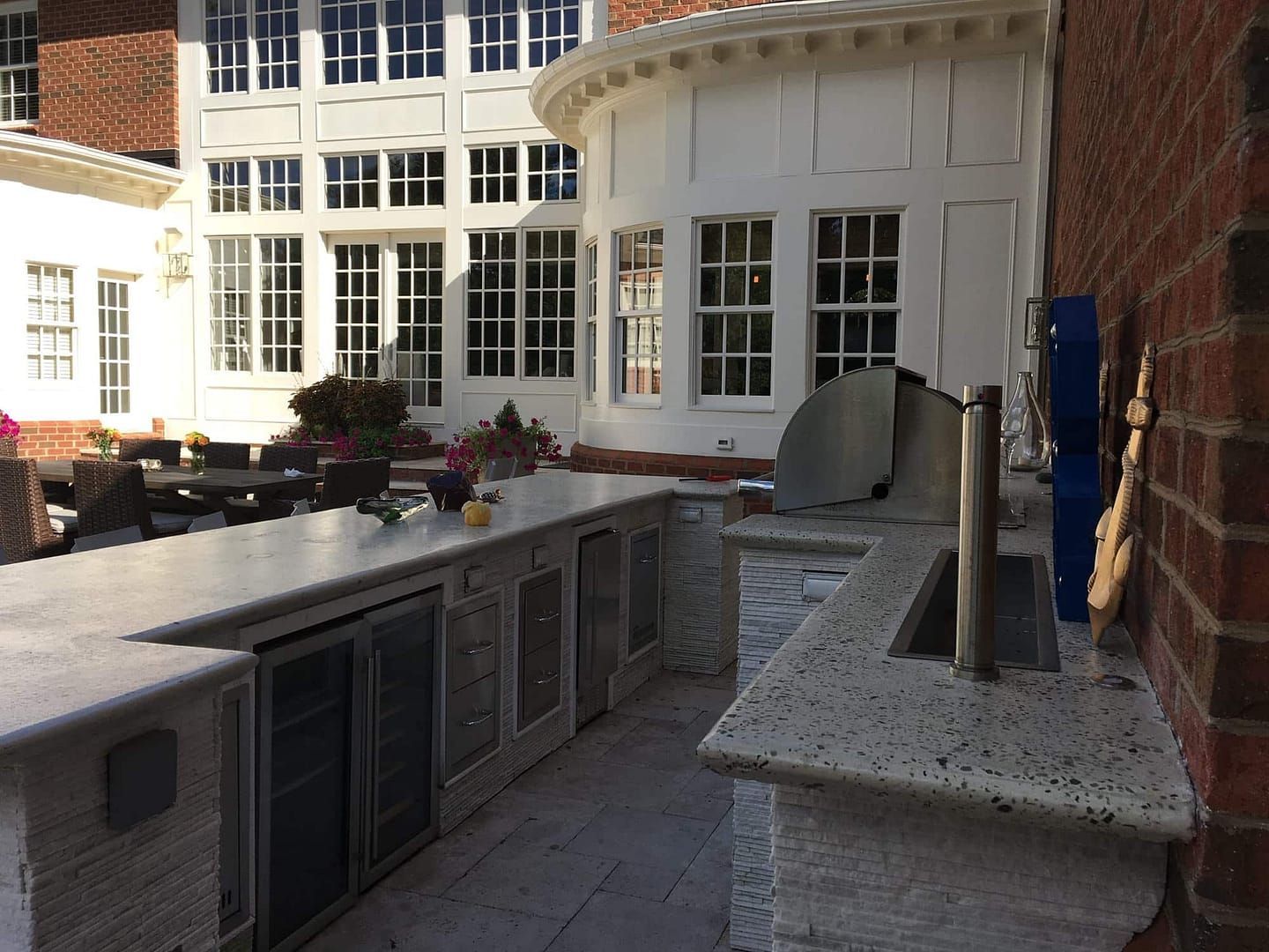 Outdoor kitchen with built-in grill, sink, and cabinets. The setting has brick and white-painted walls.