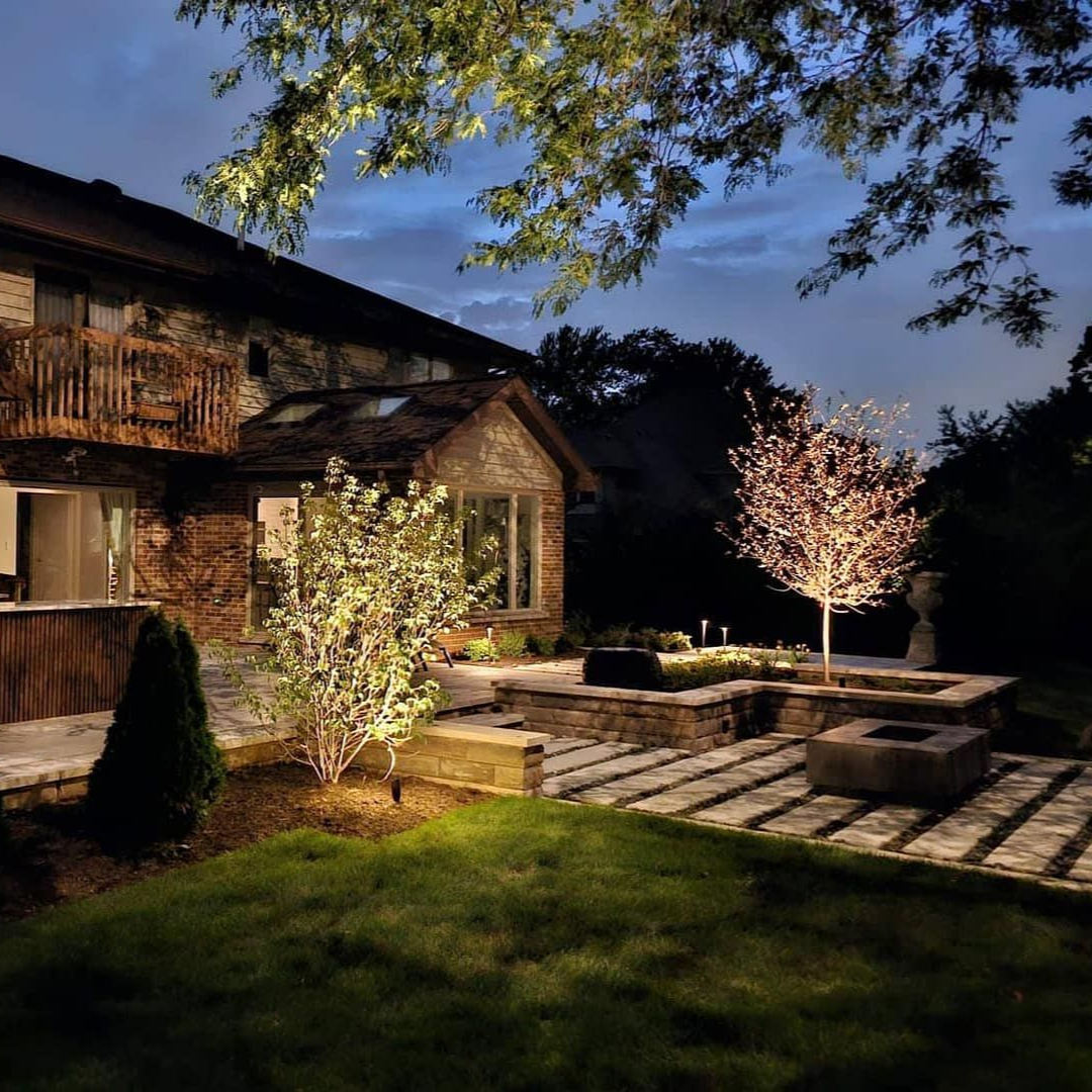 Stone house exterior with illuminated landscaping at dusk.