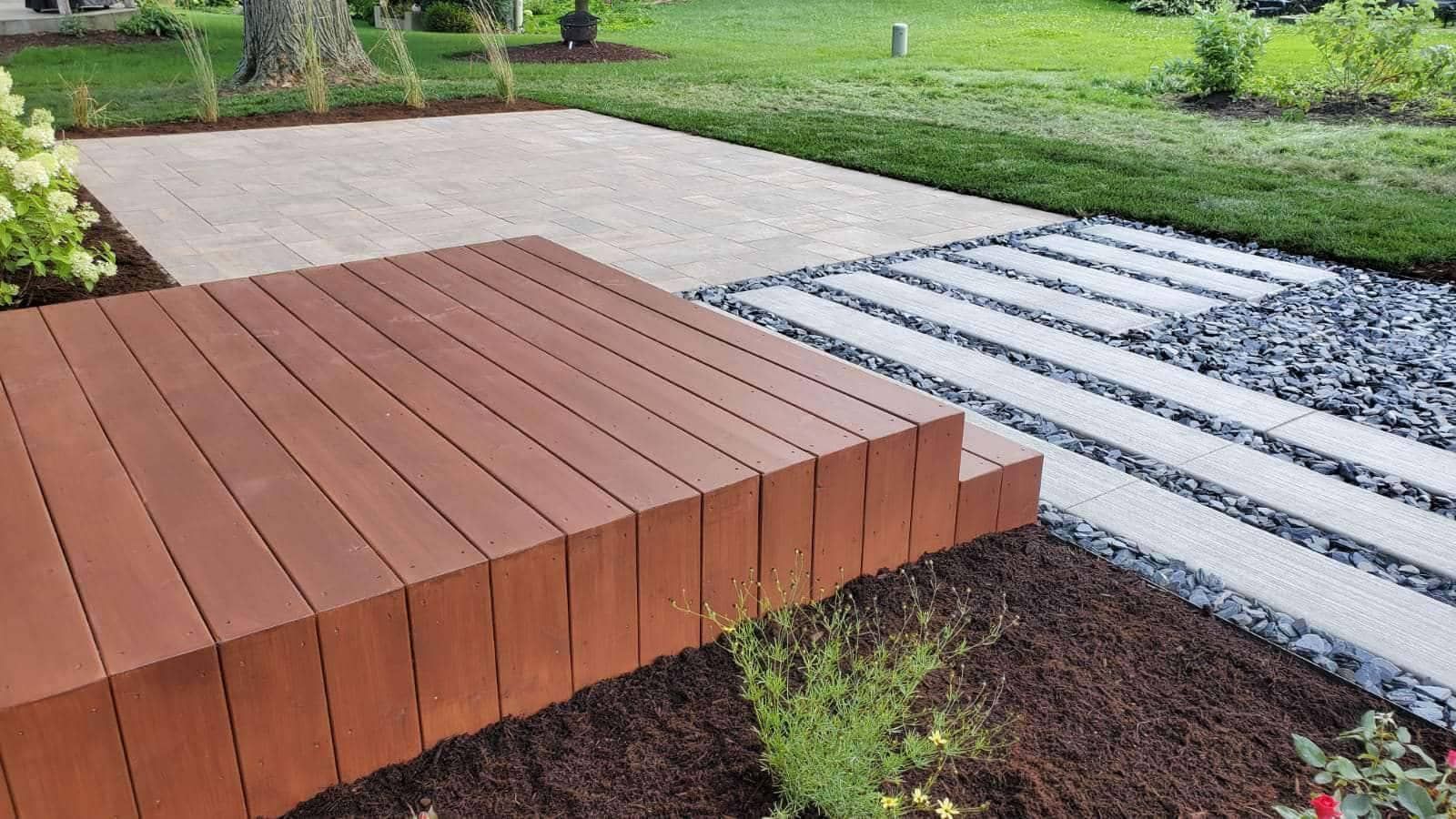 Wooden deck and stepping stones in a landscaped yard with grass and mulch.