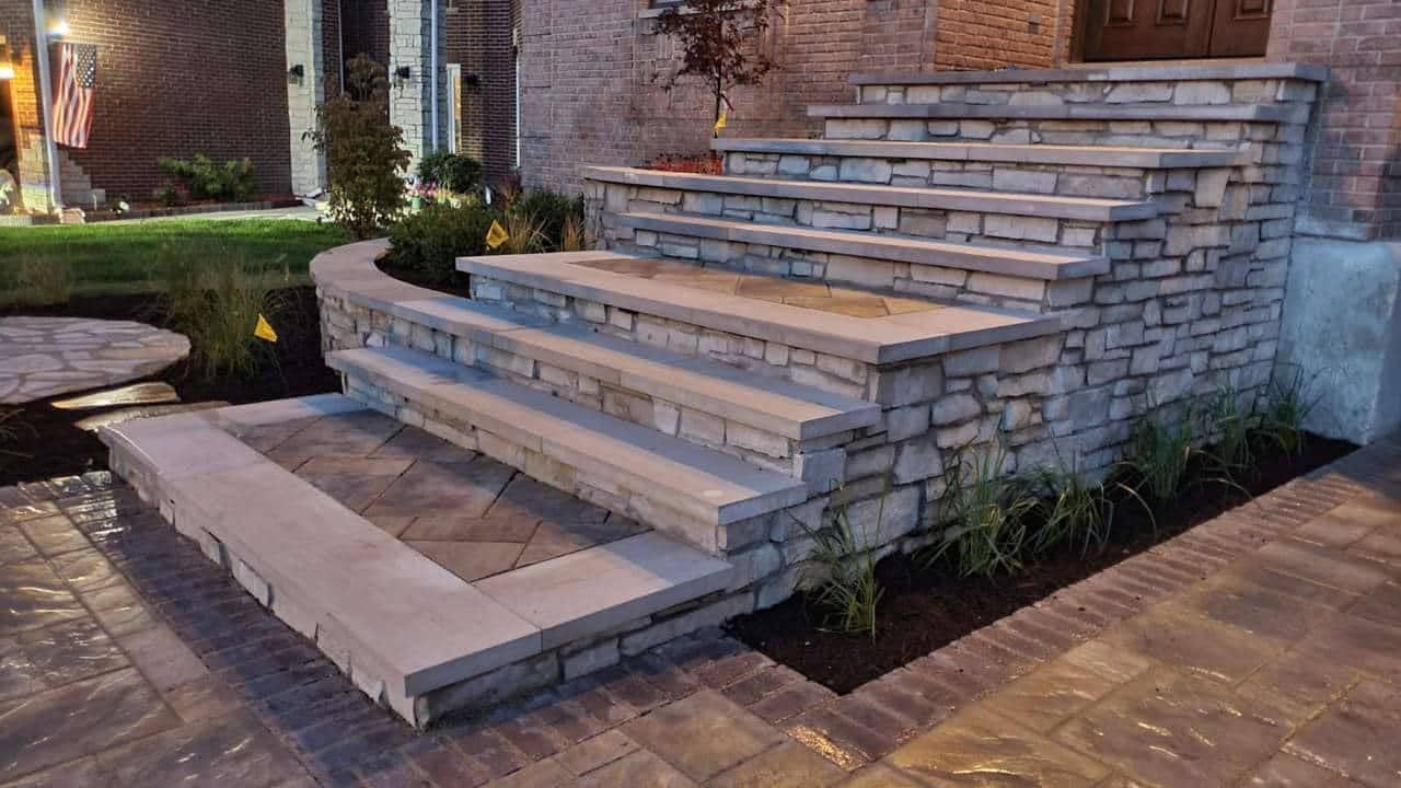 Stone steps leading up to a building, with landscaping and a paved entrance.