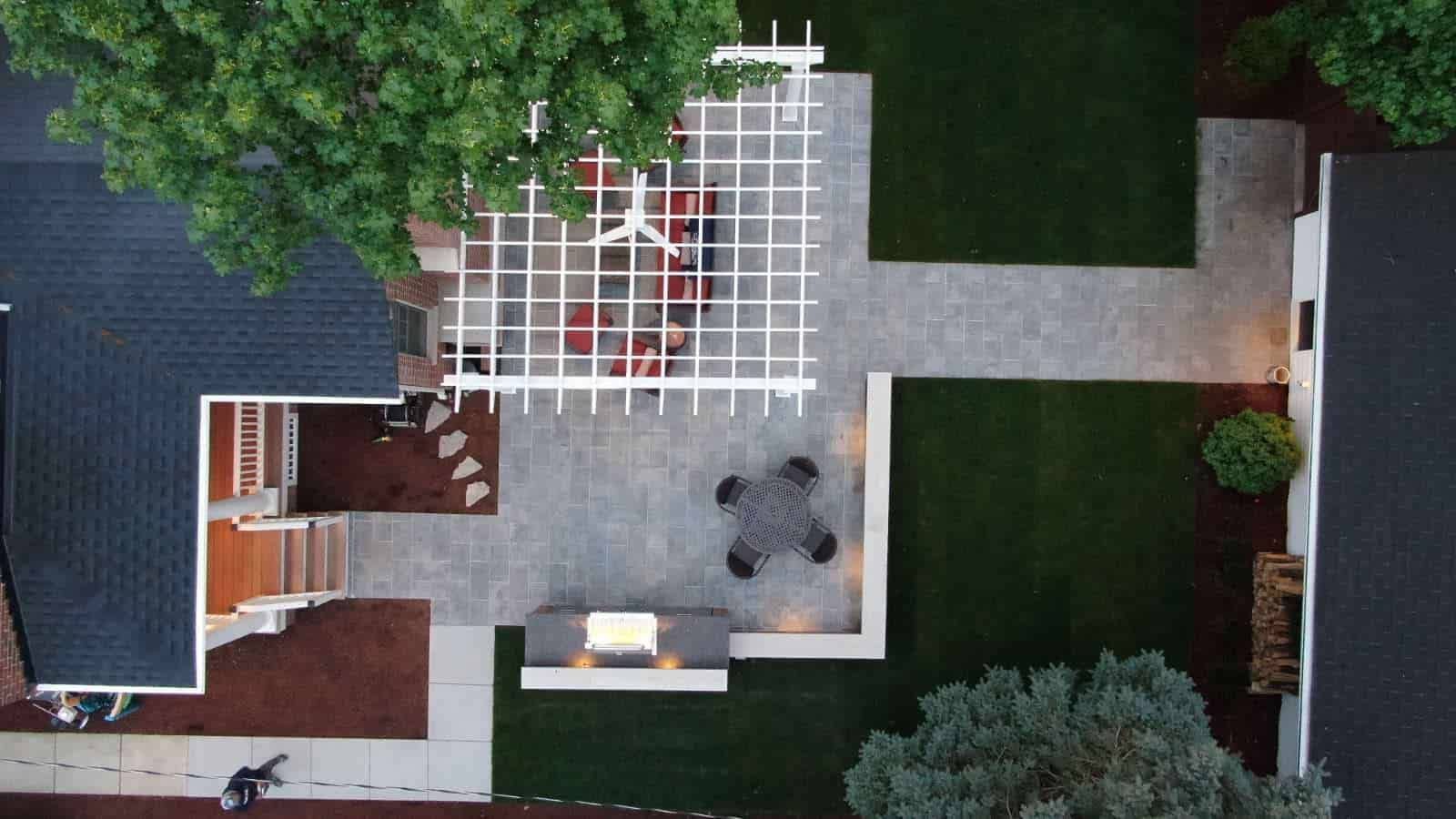Aerial view of a backyard patio with a pergola, dining area, grill, and manicured lawns.