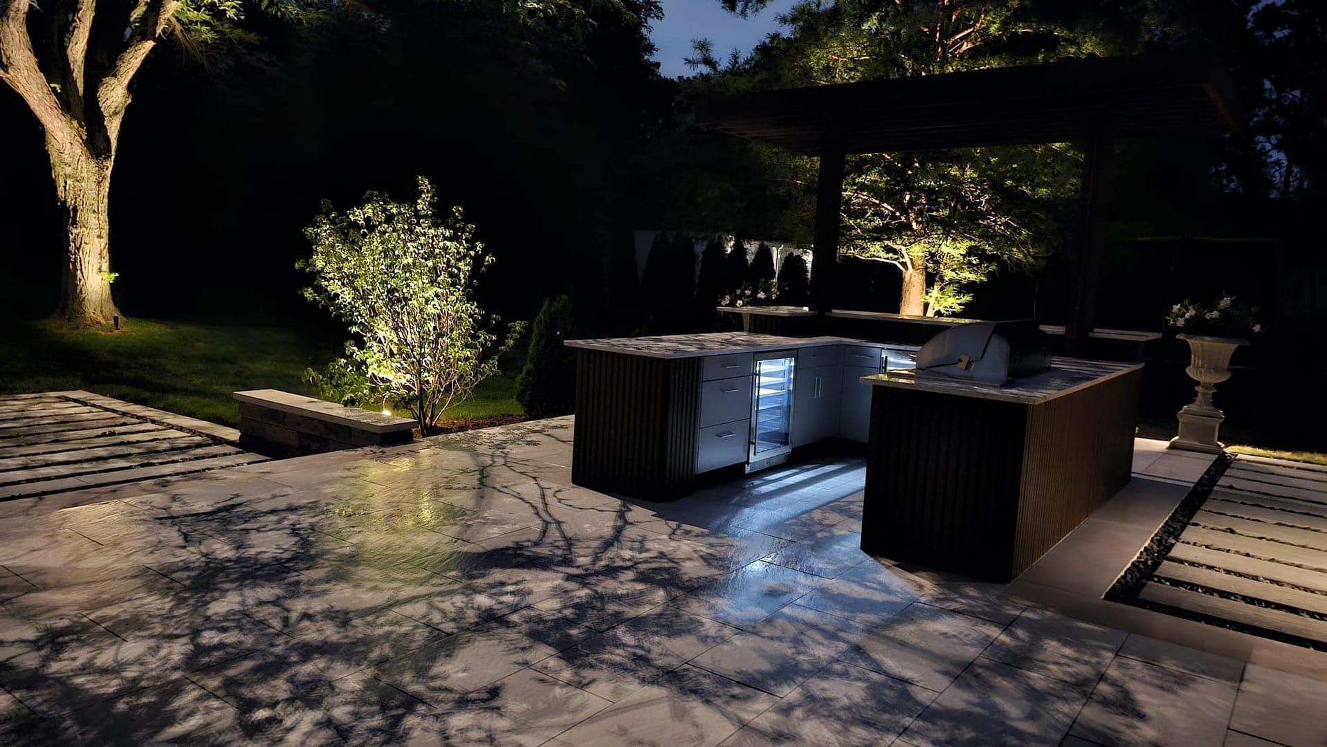 Nighttime outdoor kitchen with lit trees and stone patio.