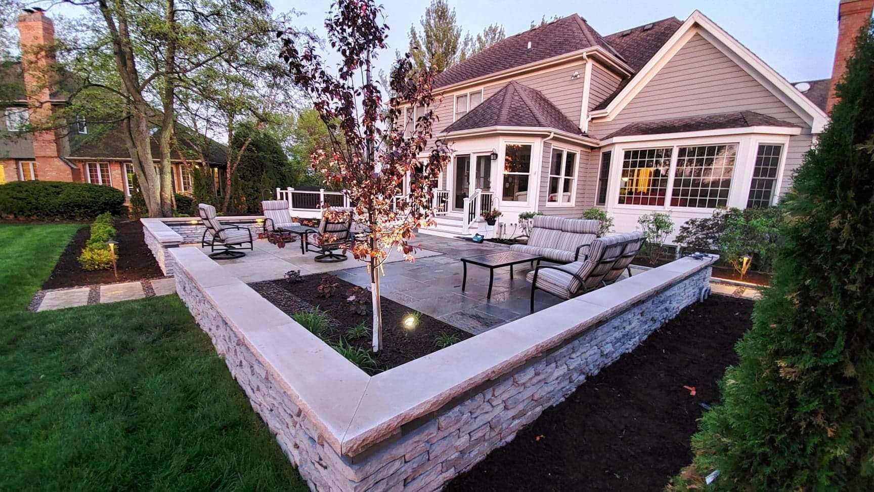 Backyard patio with seating, gray walls, and a house.
