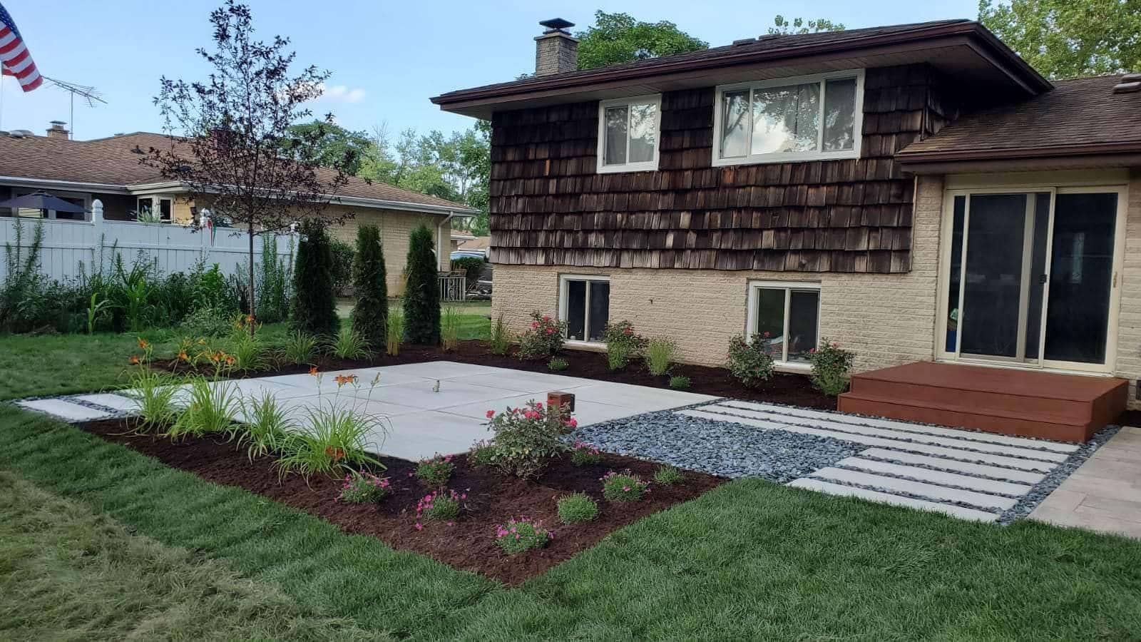 Backyard patio with pavers, gravel, and landscaping in front of a two-story house.