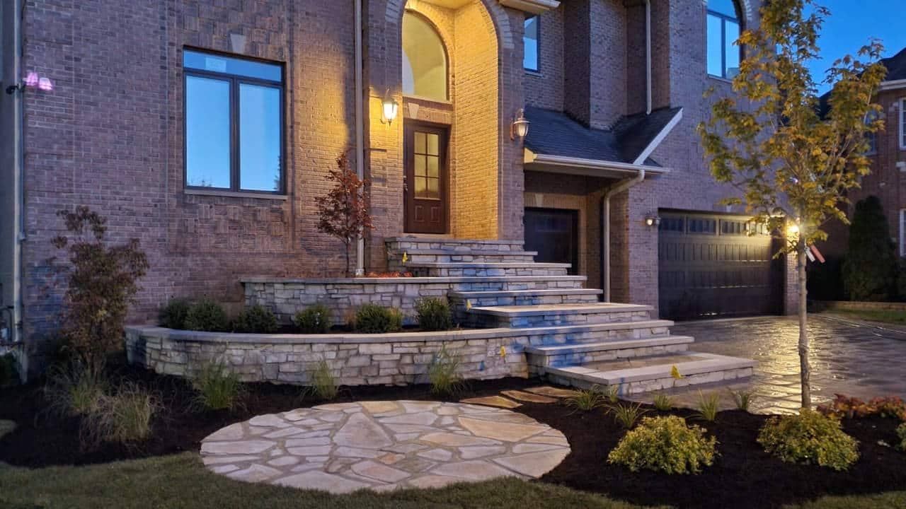 Stone steps and landscaping lead to a brick house entrance, lit by exterior lights.