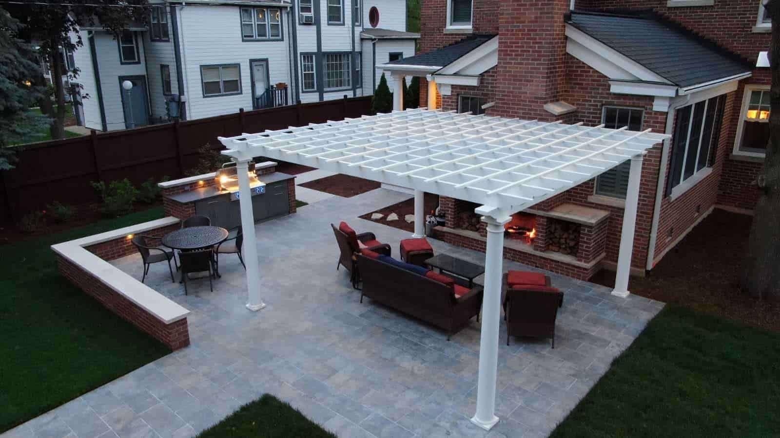 Outdoor patio with pergola, fireplace, grill, and seating in a backyard.