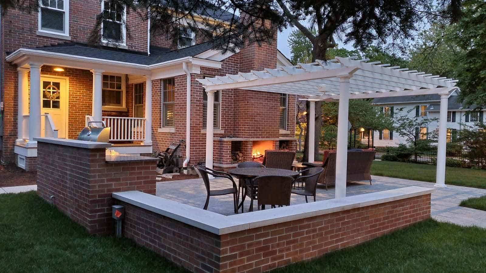 Brick patio with outdoor fireplace, pergola, seating, and a house in the background.