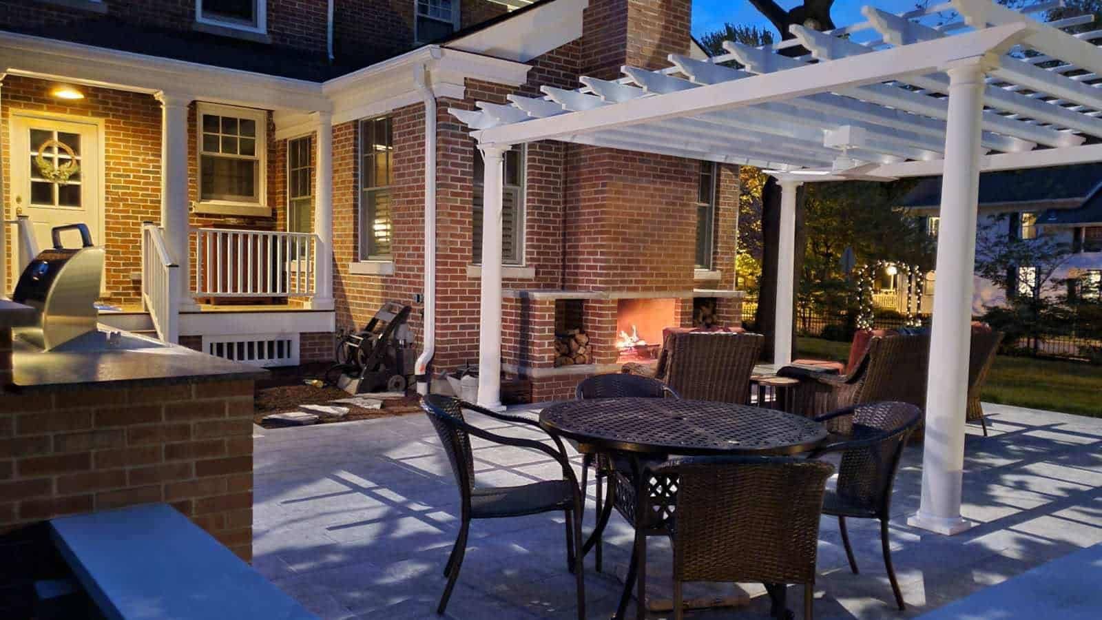 Backyard patio with pergola, fireplace, and seating. Evening view, blue tones, cozy.