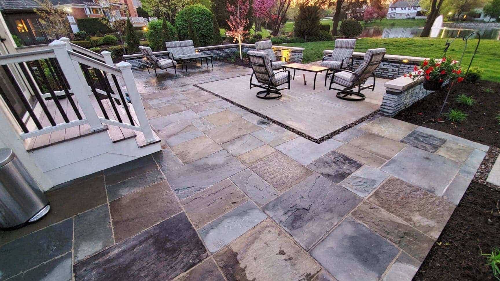 Stone patio with outdoor furniture, steps, and a view of a lake at sunset.