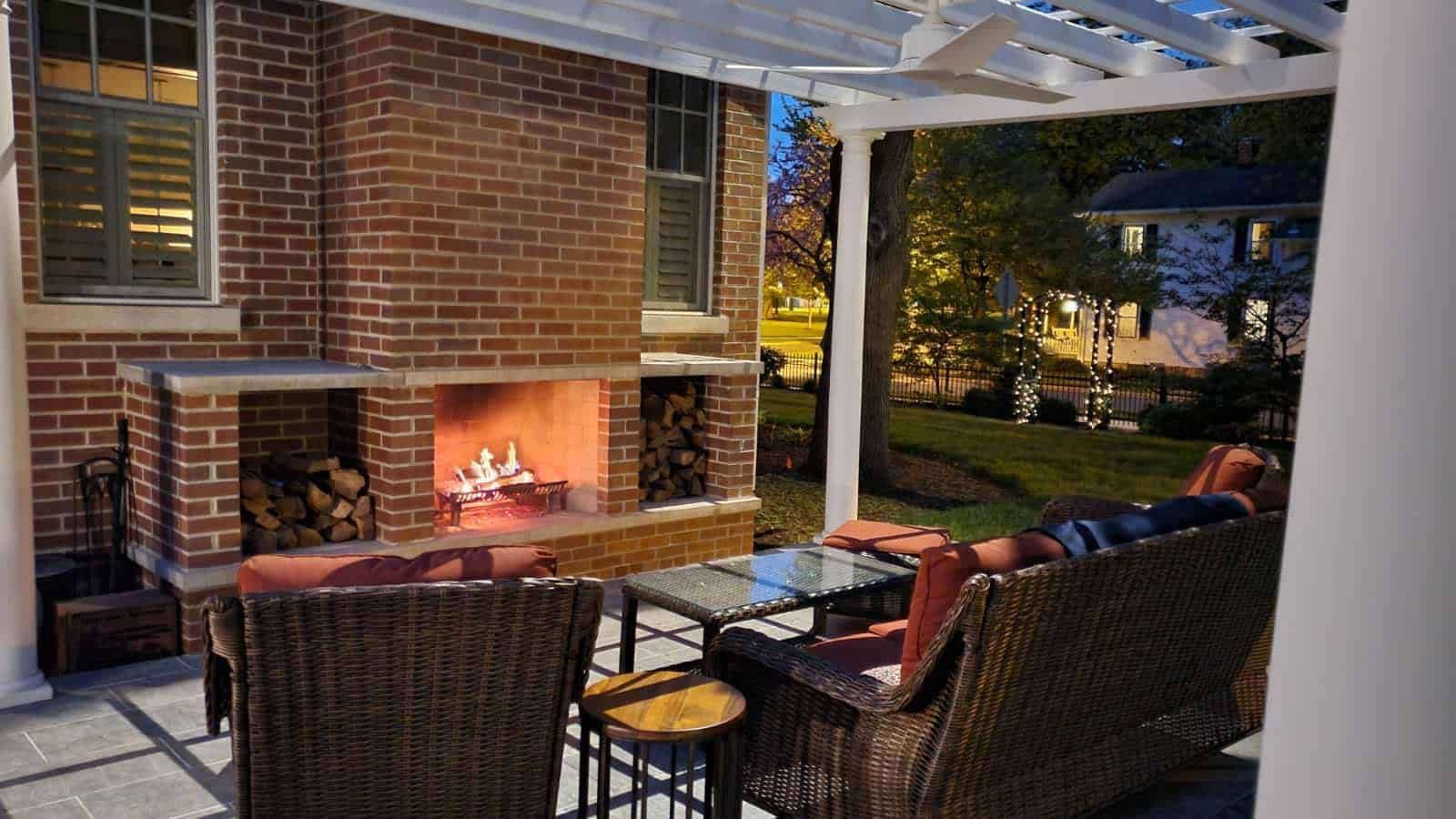 Outdoor patio with brick fireplace and wicker furniture. Fire glowing, night scene.