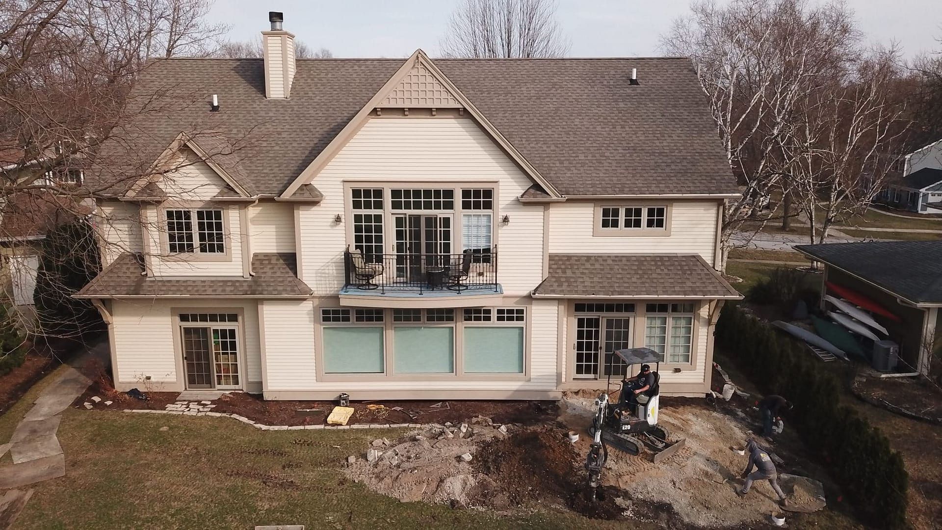 Beige two-story house with balcony and people in front on a sunny day.