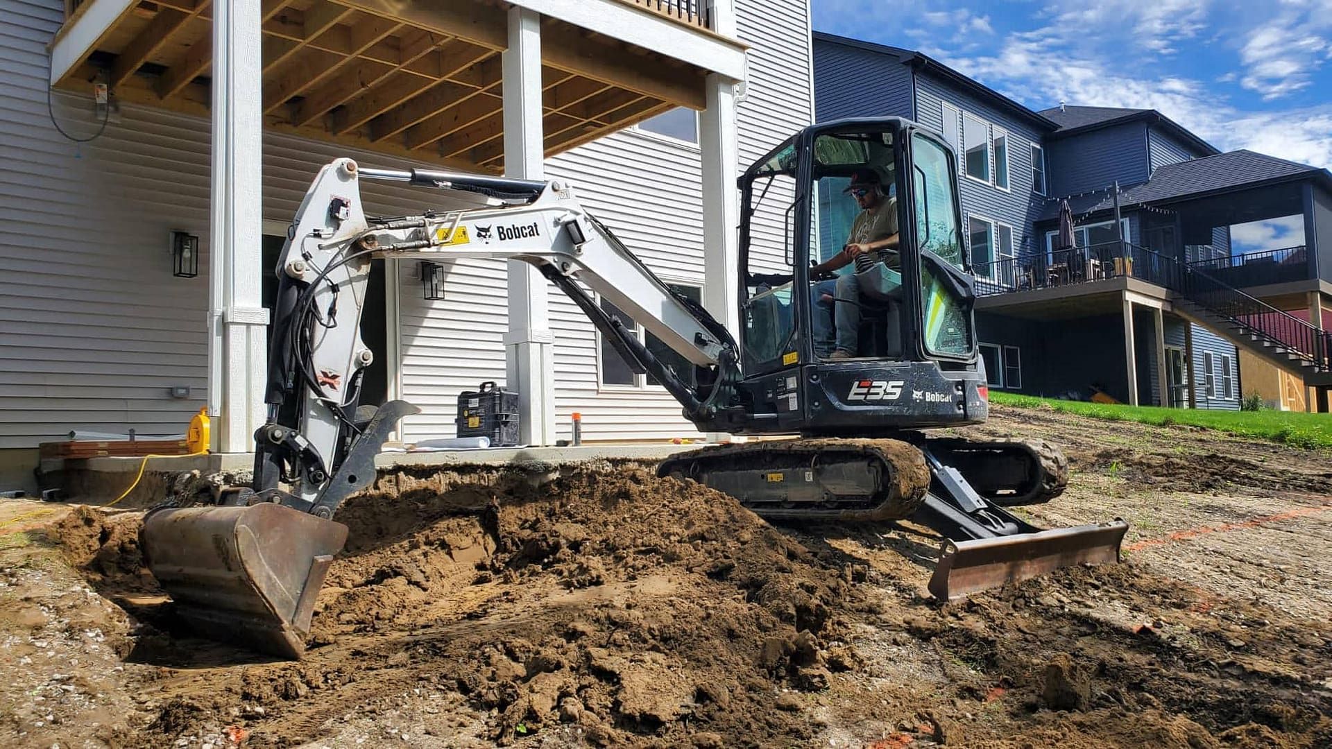 Mini excavator digging near a house with a blue sky.