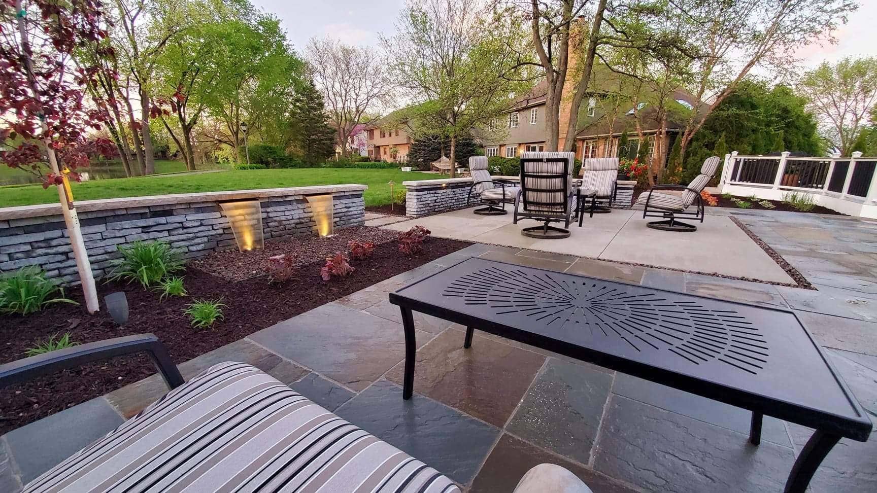 Outdoor patio with dark table, seating, landscaping, and trees.