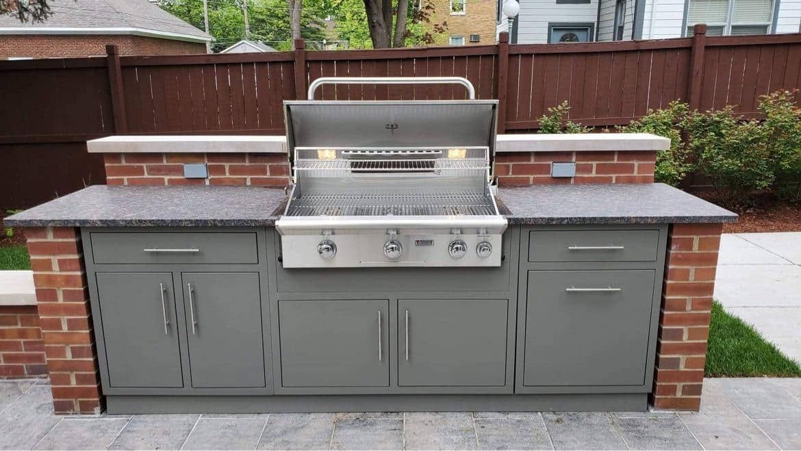 Outdoor kitchen with gray cabinets, a stainless steel grill, and red brick accents.