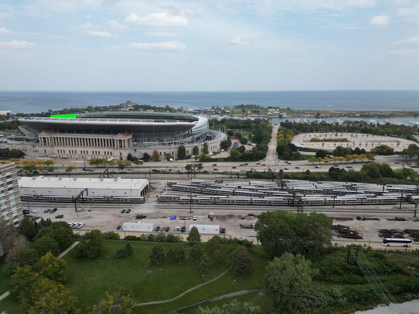 Aerial view: Stadium, train yard, lake, and park under a blue sky.