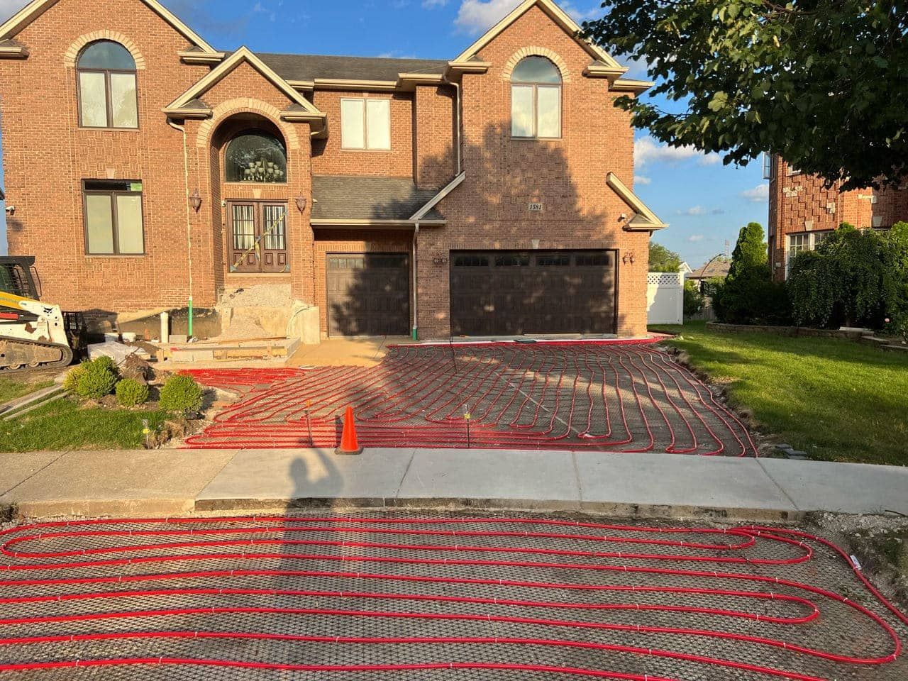 Red tubing laid on driveway in front of a brick house, for a radiant heating system.