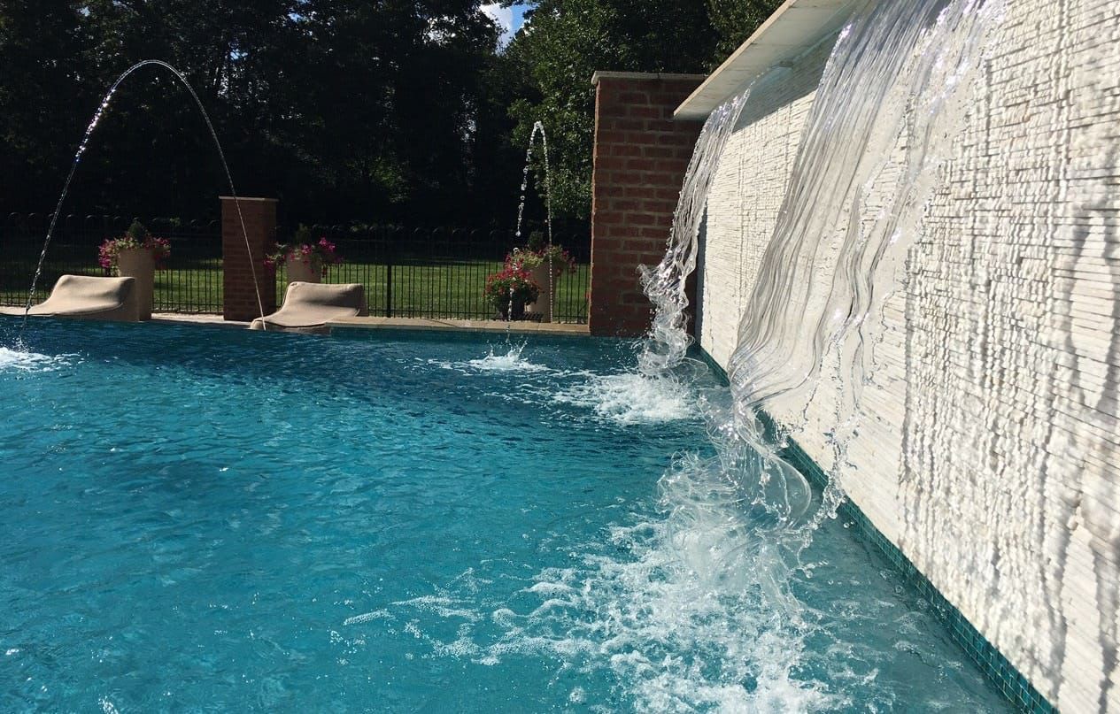 A blue pool with a waterfall feature, clear water splashing down. Sunny day.