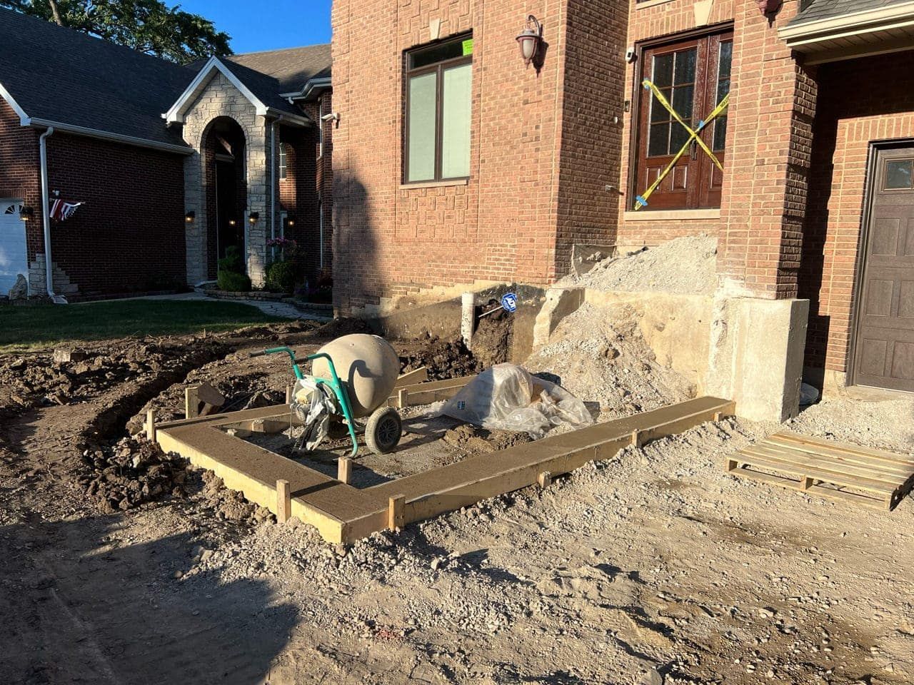 Construction site with a brick house. Forms for concrete are set up near a cement mixer.