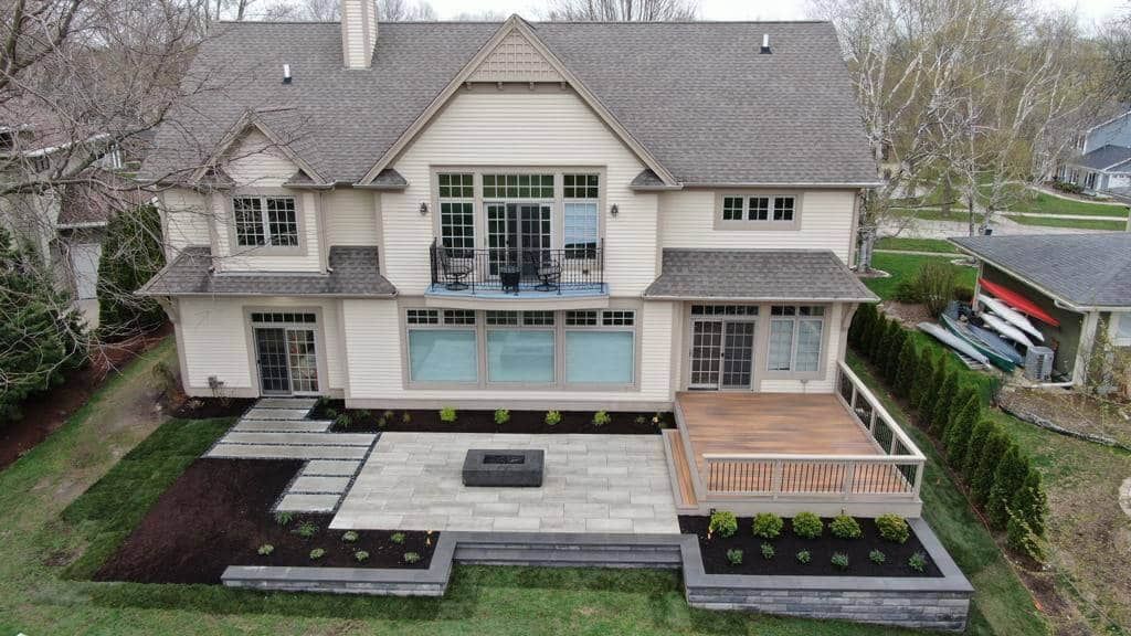 Back view of a two-story beige house with a deck, patio, fire pit, and landscaping.