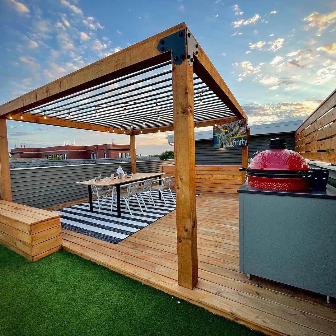 Rooftop deck with a grill, pergola over dining table, and artificial turf. Sunset colors, modern design.