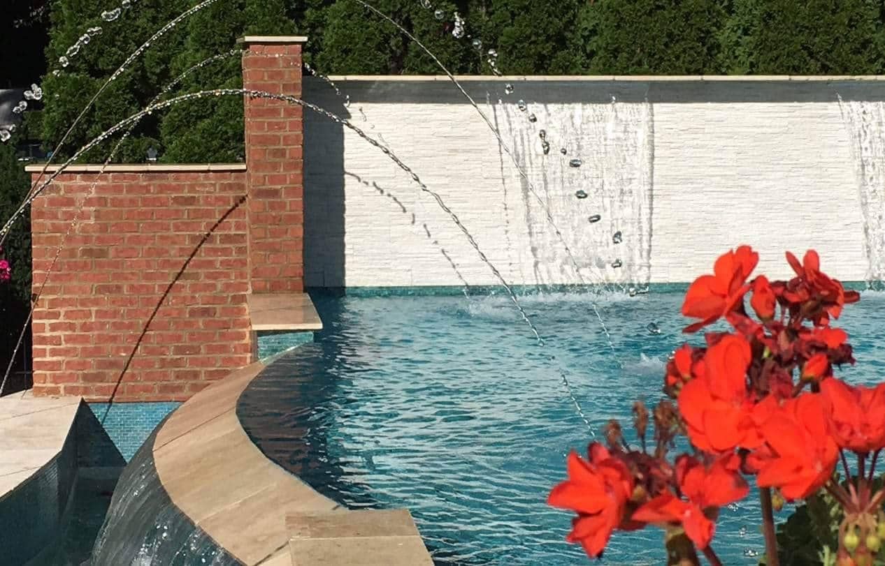 Pool with water features: waterfall, jets, red brick, and flowers.