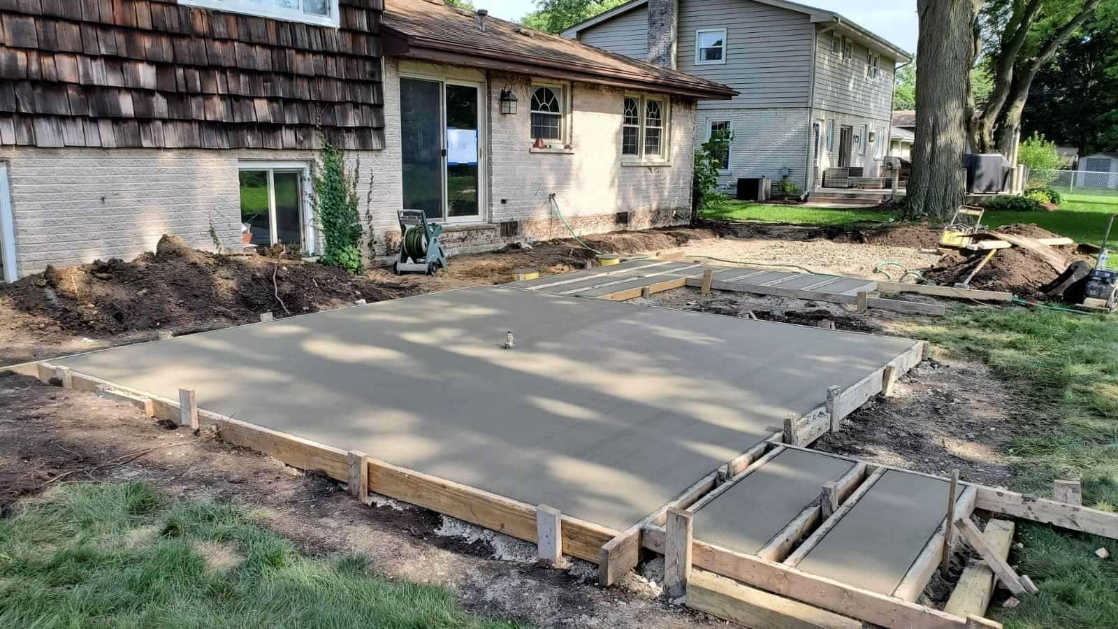 Newly poured concrete patio with wooden framing in a backyard.