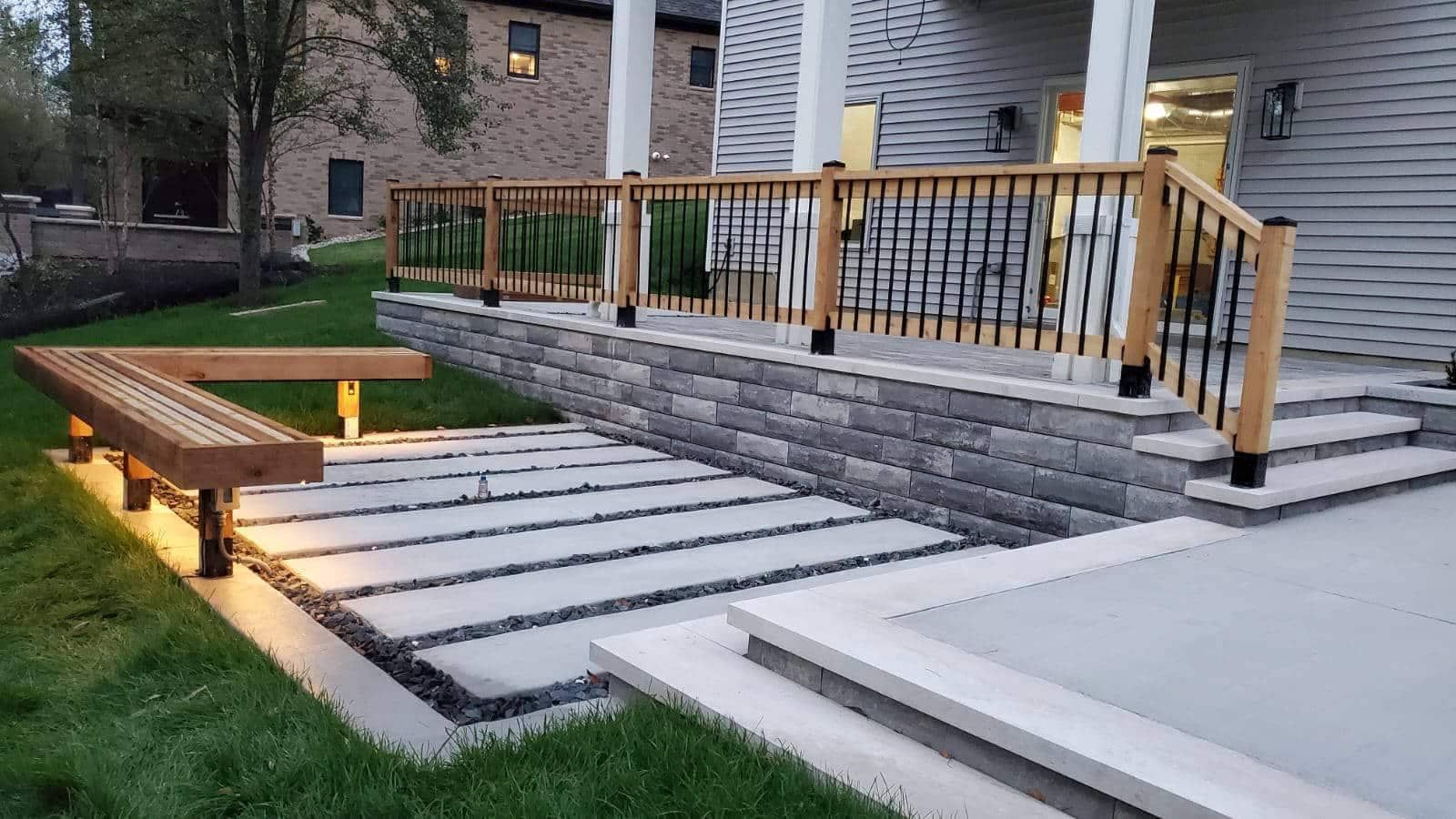 Backyard patio with stone steps, built-in bench, and wooden railing along a porch.