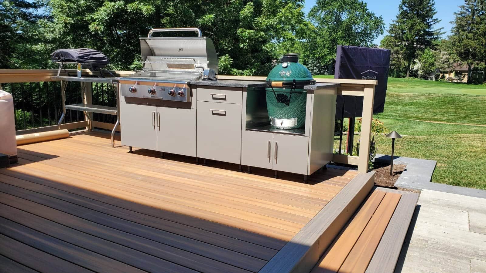 Outdoor kitchen on a wooden deck with a gas grill, Big Green Egg, and cabinetry.