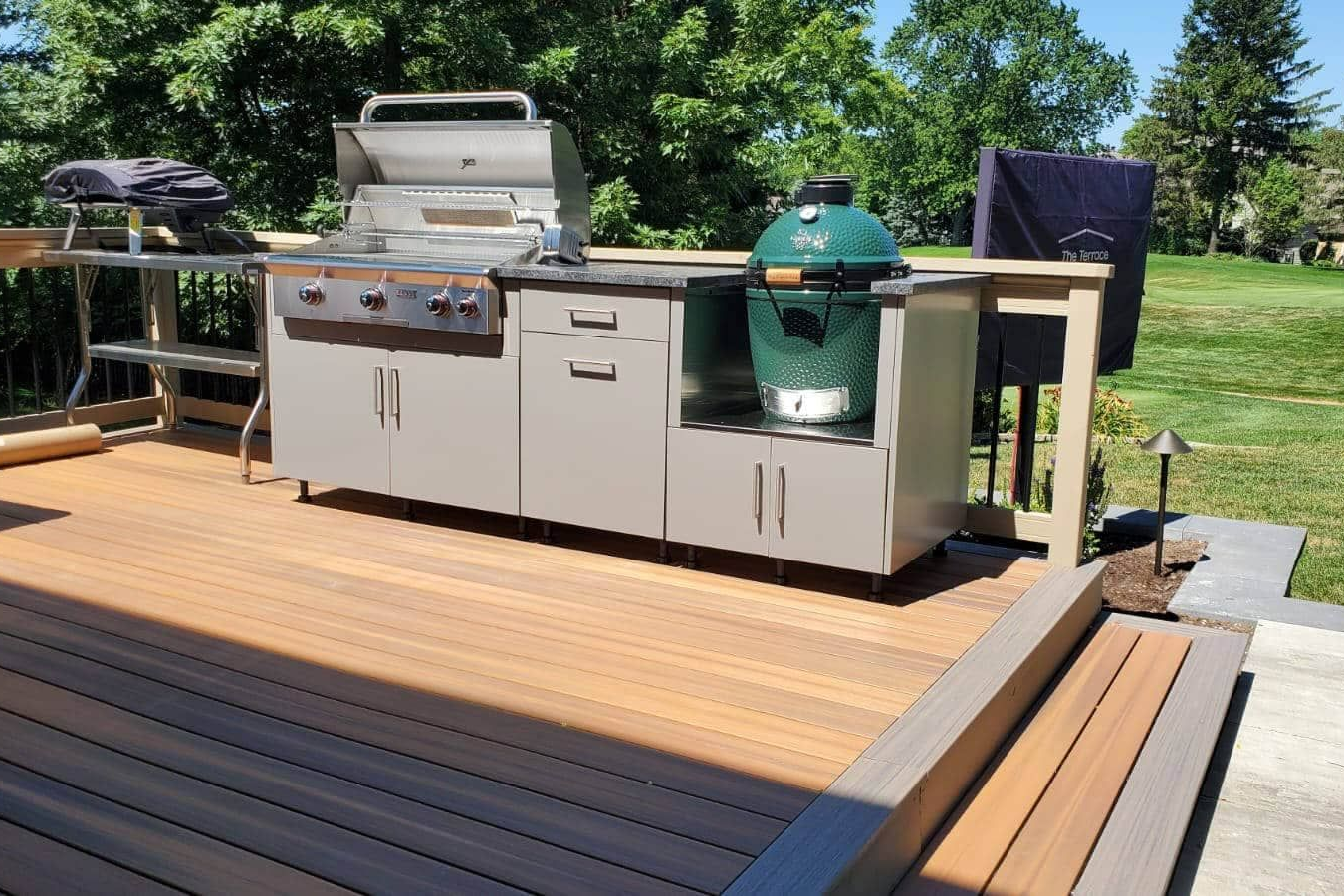 Outdoor kitchen with grill, Big Green Egg, and cabinets on a wooden deck.