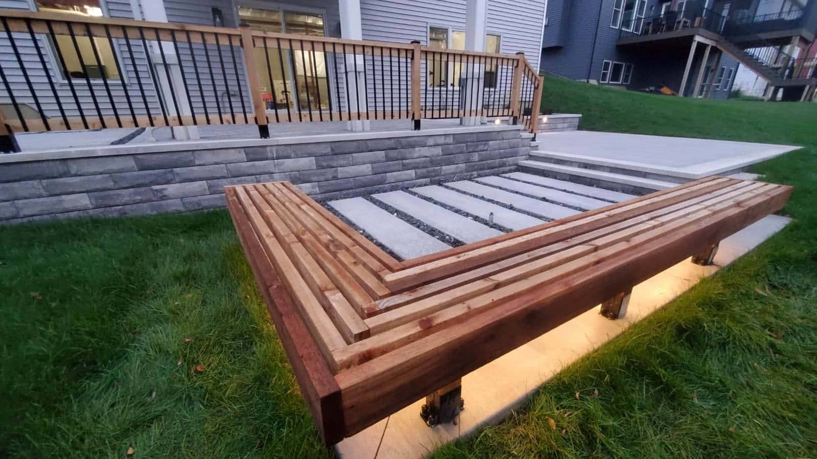 L-shaped wooden bench with built-in lighting on a grassy yard, adjacent to a stone patio and deck.
