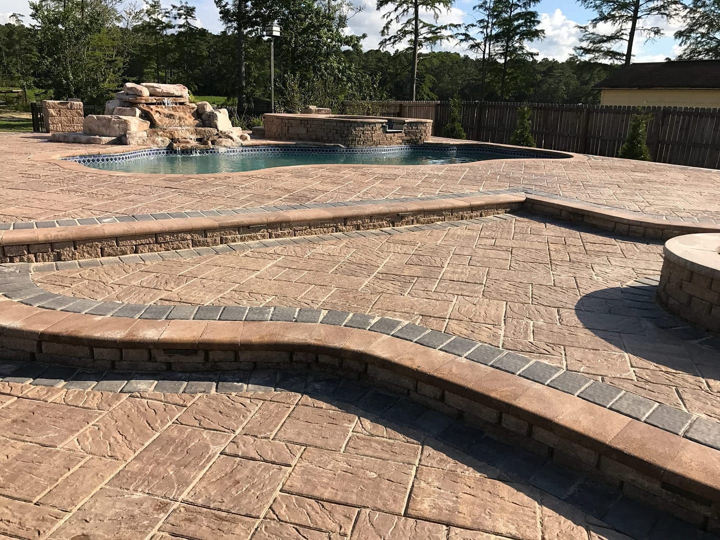 Brick patio with pool, waterfall, and fire pit; brown and tan tones.