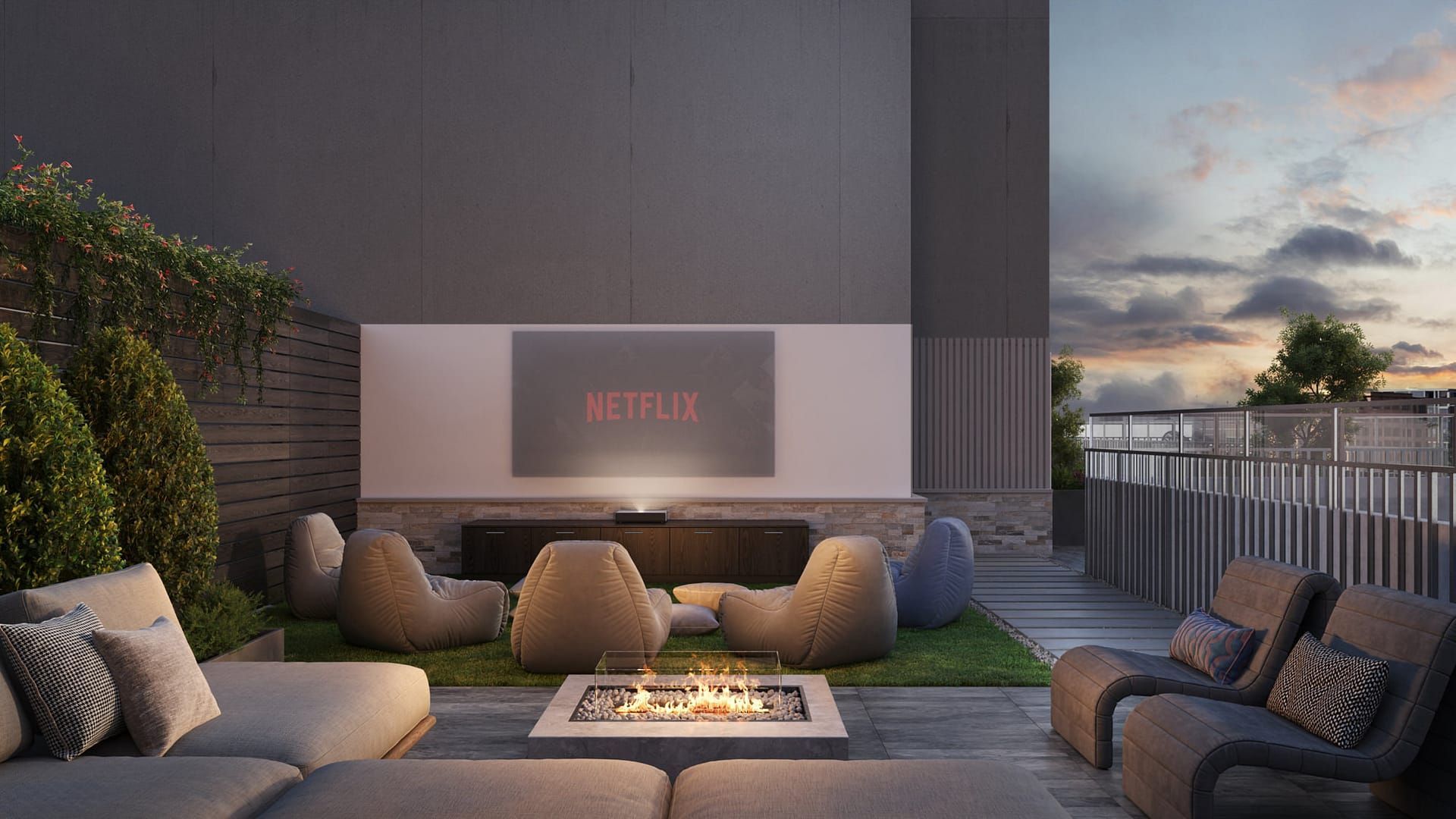 Outdoor rooftop cinema with a screen, bean bag chairs, sofas, fire pit, and greenery.
