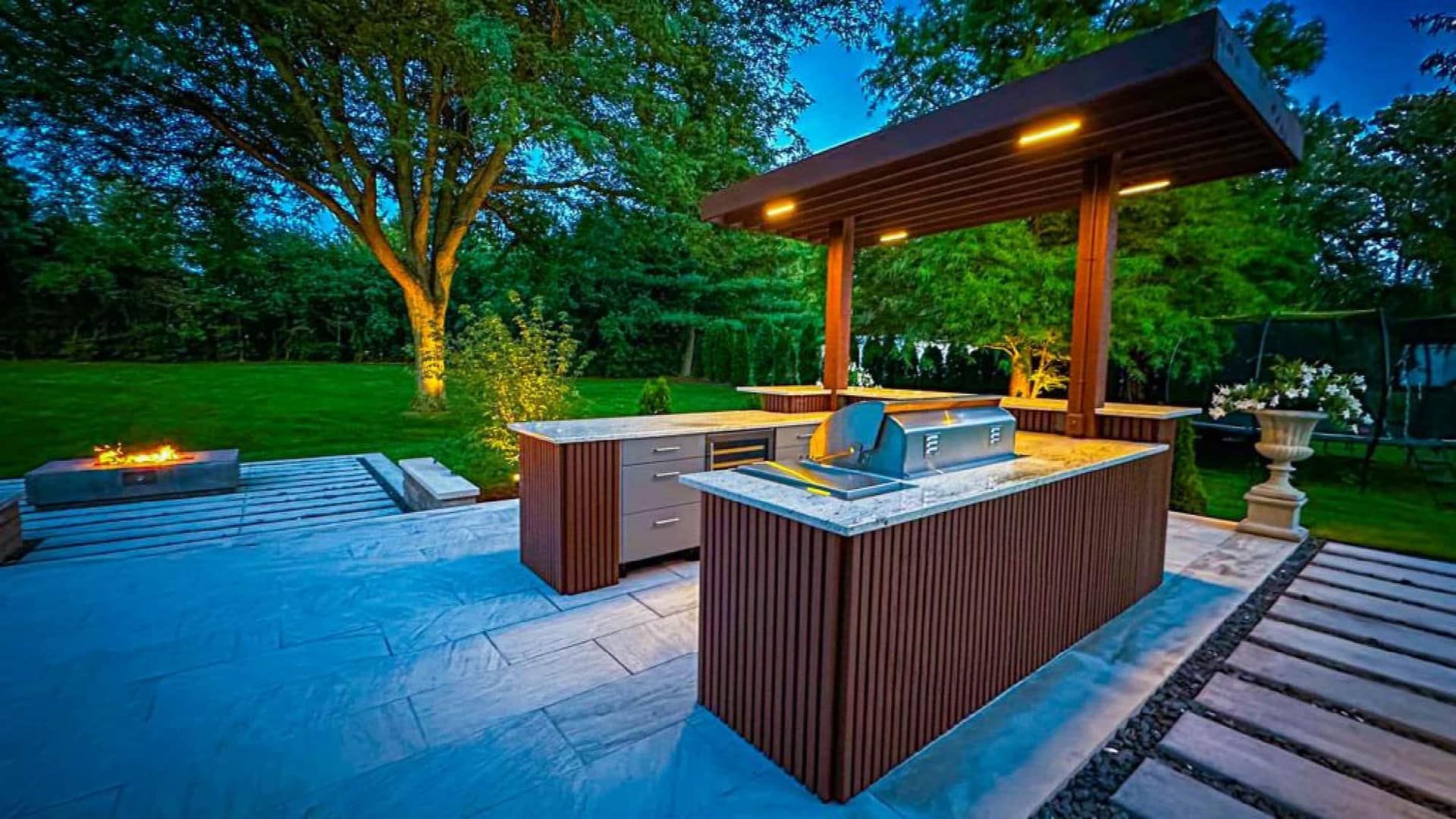 Outdoor kitchen with brown cabinets, a grill, and a canopy lit with overhead lights.