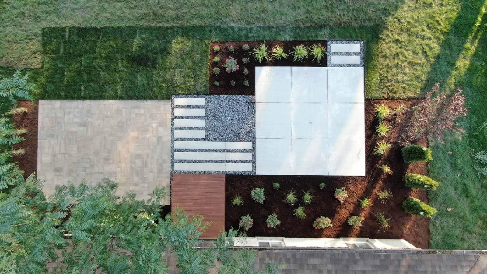 Overhead view of a modern landscaped yard with grass, pavers, gravel, and plants.
