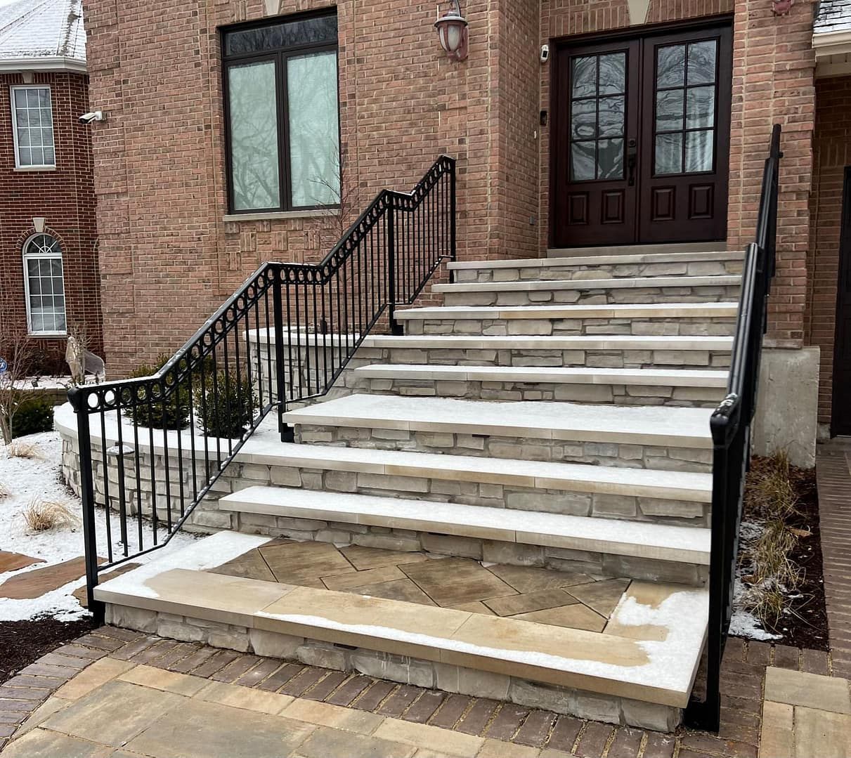Stone steps with black railing leading to a brick building entrance, lightly covered in snow.