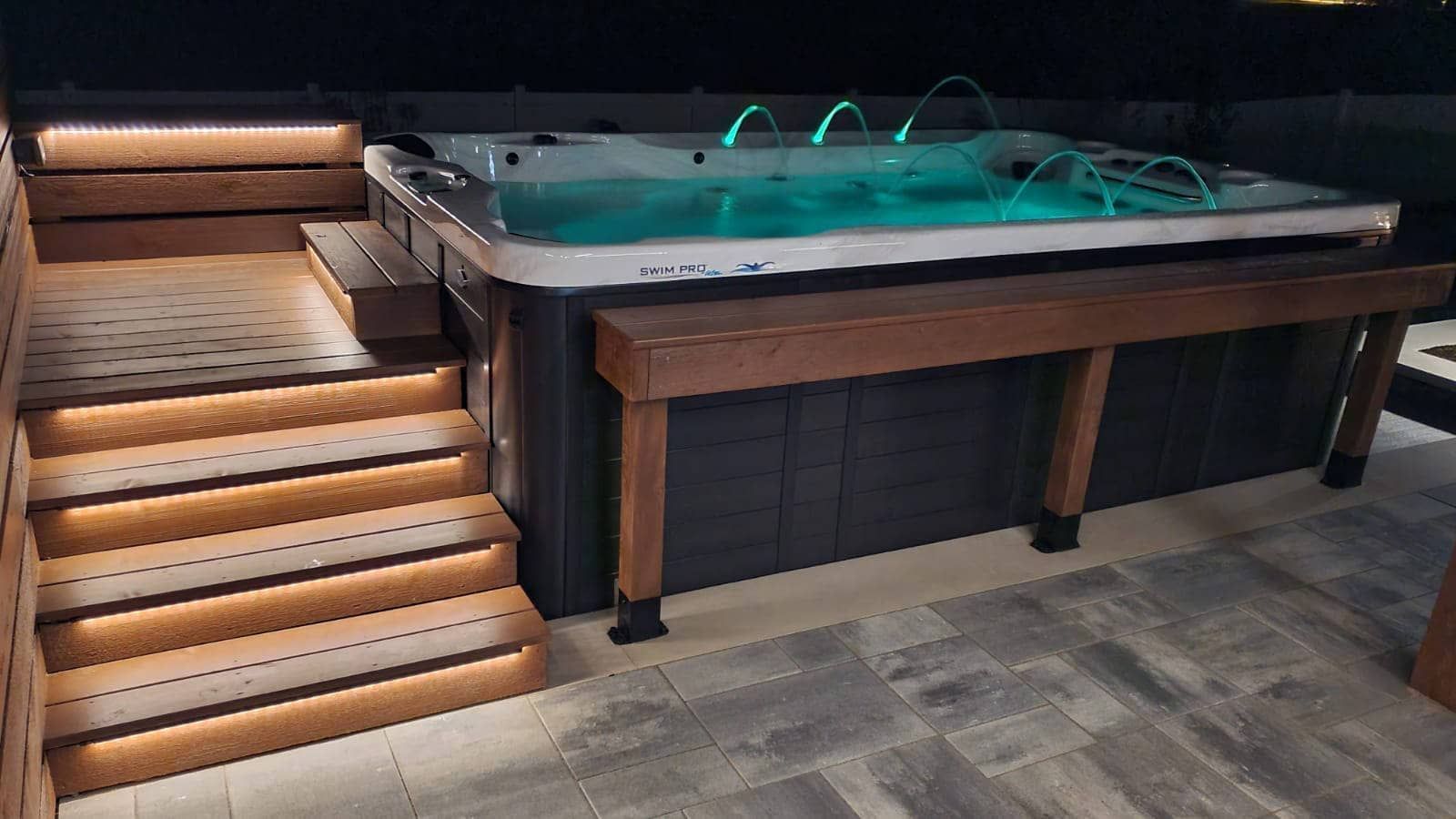 A lit hot tub at night with steps, wooden accents, and illuminated jets.