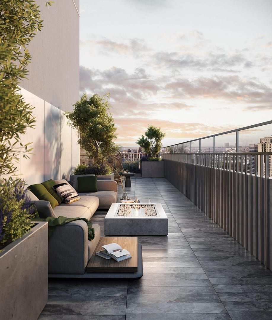 Rooftop patio with modern grey sofa, fire pit, and cityscape view at sunset.