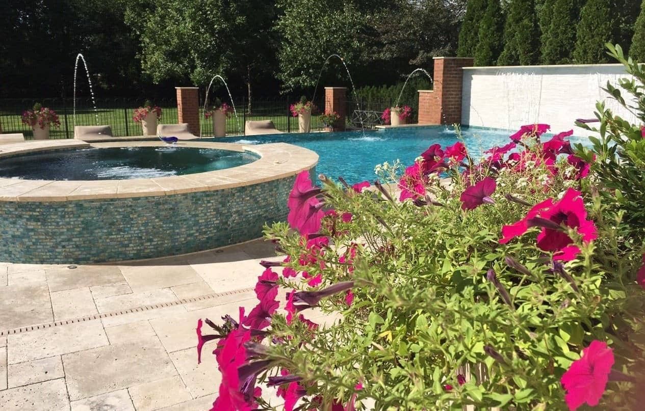 Pool with a jacuzzi, fountains, and flowers; sunny outdoor setting.