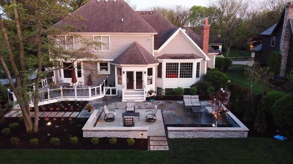 Backyard patio with seating and a fireplace, adjacent to a two-story house.