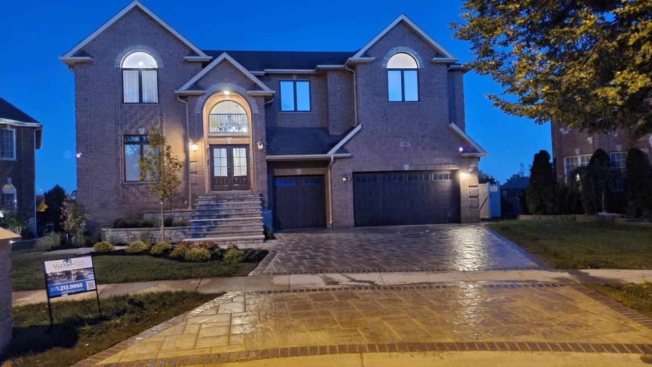 Brick house at dusk with lit windows and a patterned driveway.