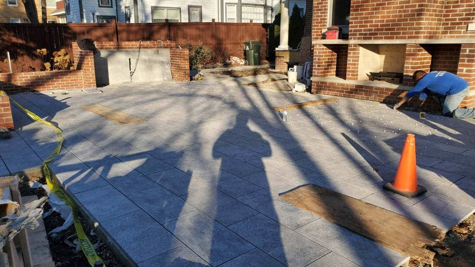 Construction site with workers laying paving stones; brick fireplace and backyard setting.