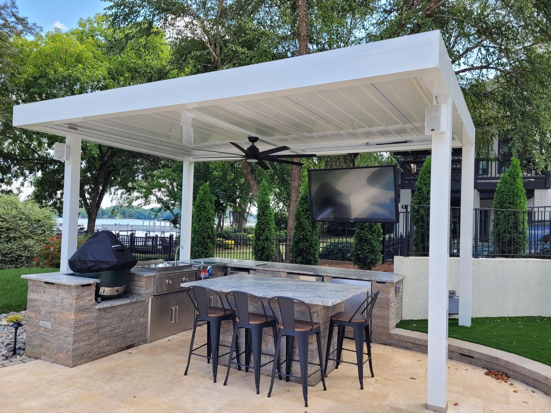 Outdoor kitchen with white pergola, built-in grill, bar seating, and a mounted TV.