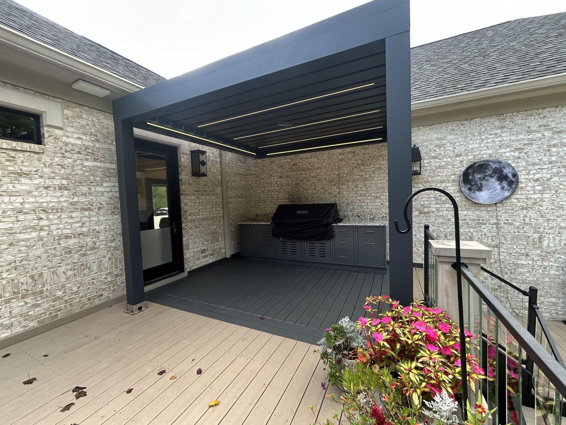 Dark gray pergola over an outdoor kitchen on a deck, featuring a grill and built-in cabinetry.