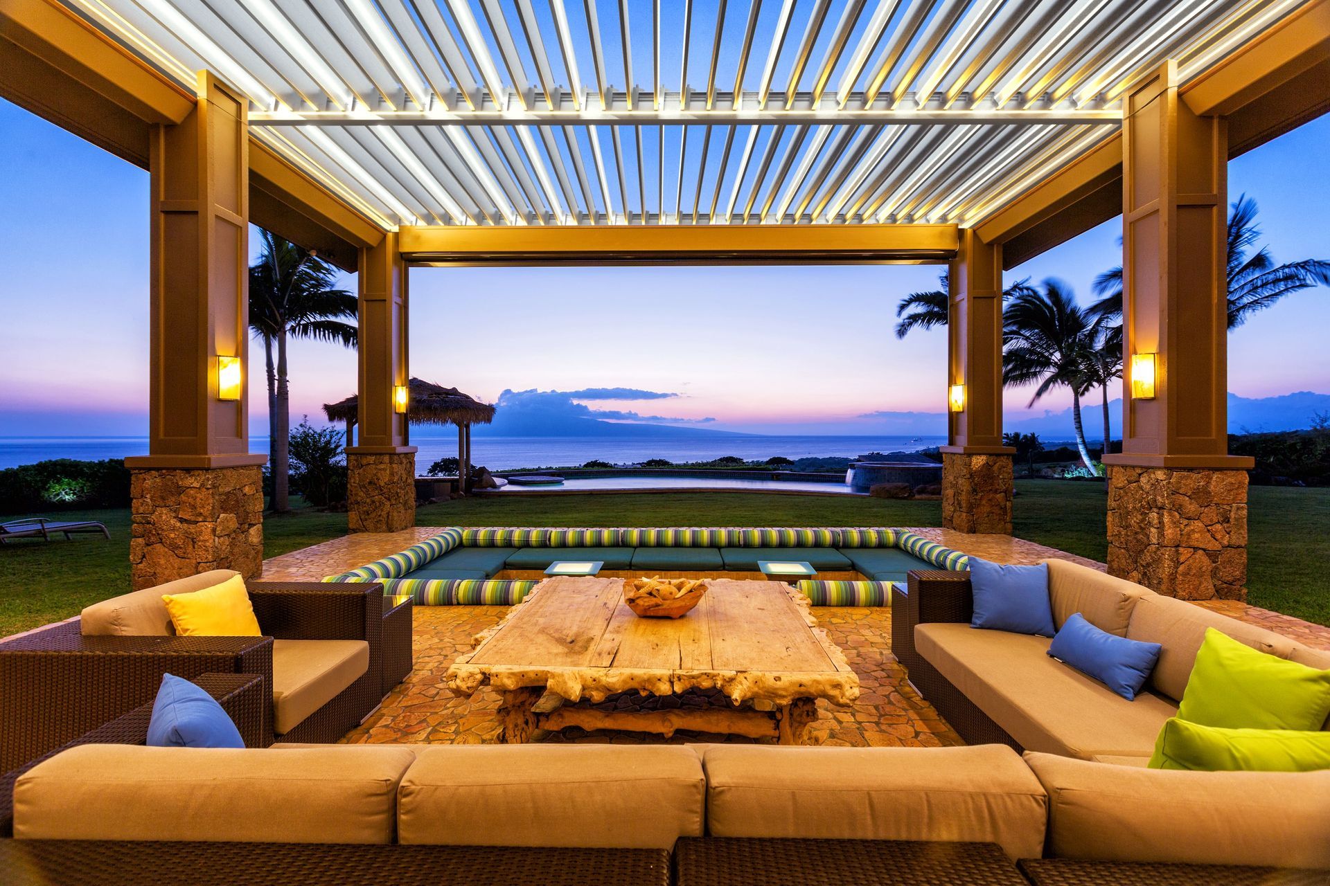 Outdoor lounge with sofas, coffee table, and ocean view at sunset.