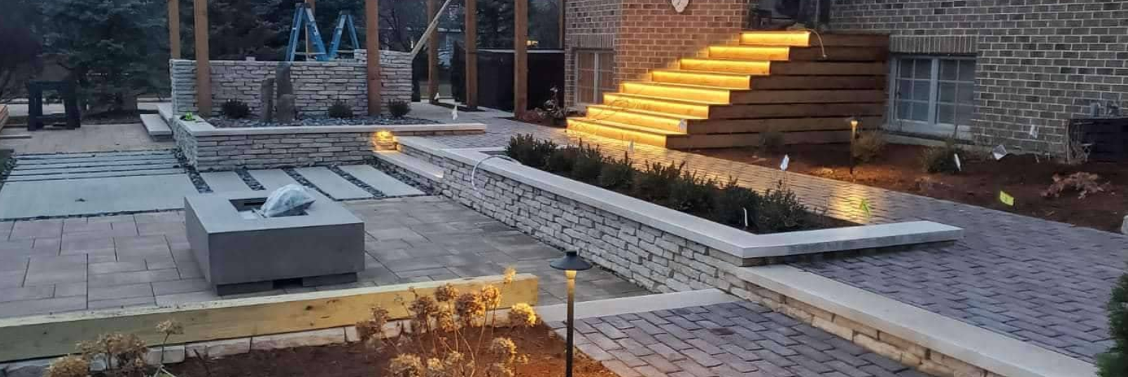A modern outdoor patio with illuminated steps, stone walls, and a fire pit.