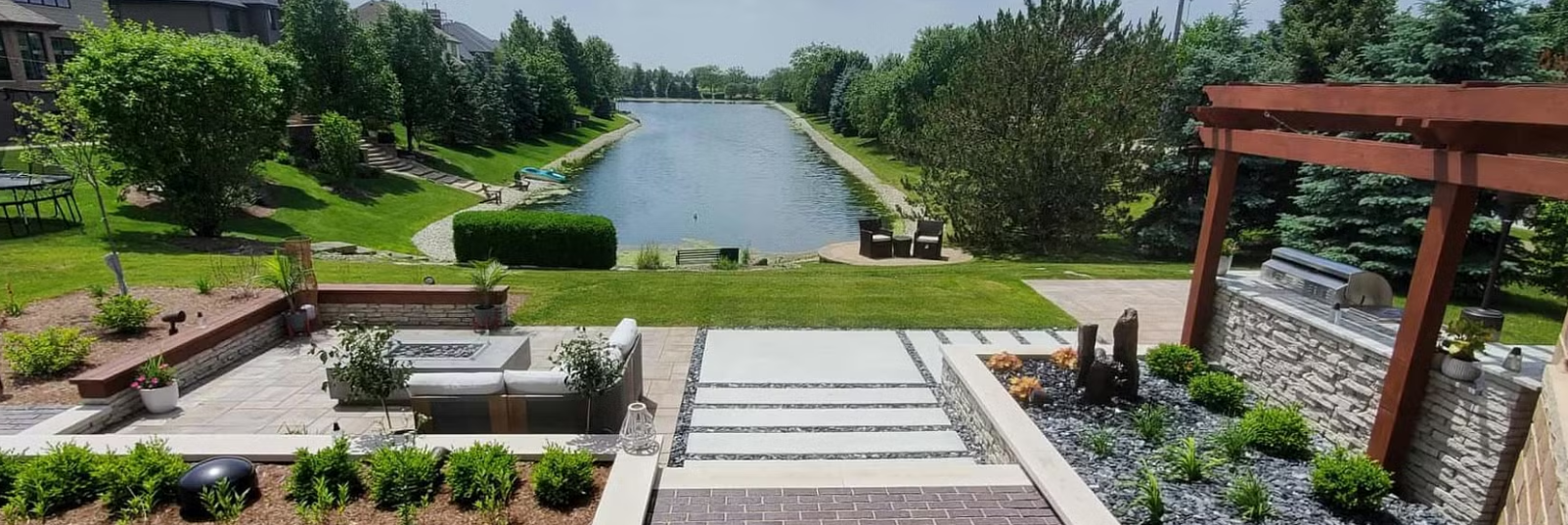 A spacious patio overlooks a long body of water. Stone steps lead down to a sunken seating area.