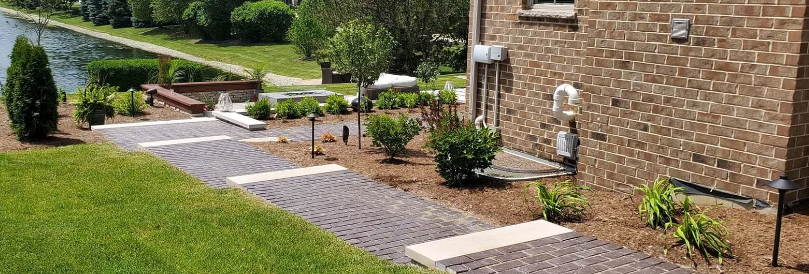 Brick house with a landscaped path, lawn, and a canal in the background.