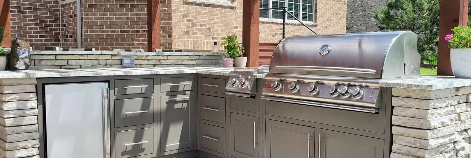 Outdoor kitchen with a grill, refrigerator, and stone counters.
