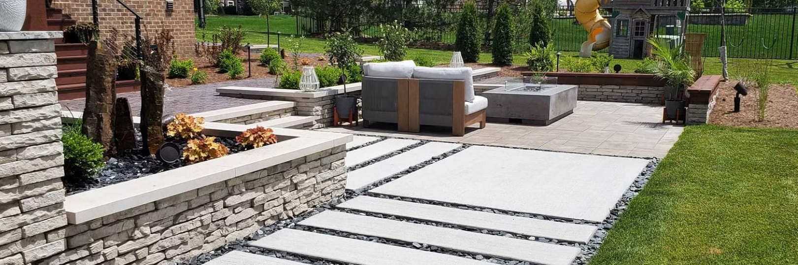 A modern backyard with a stone walkway, seating area, and landscaping.