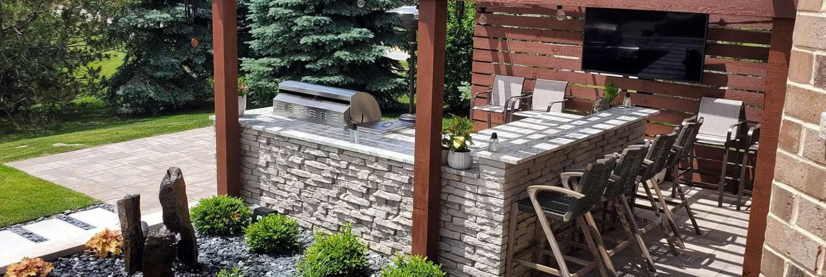 Outdoor kitchen with a grill, bar, and TV, under a wooden pergola.